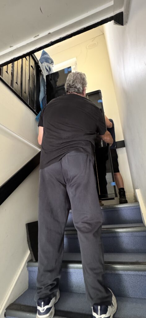 Professional piano movers carefully moving an upright piano upstairs using specialist equipment.