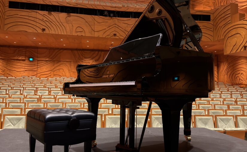 Professional piano movers positioning a Kawai grand piano on stage for a concert performance.