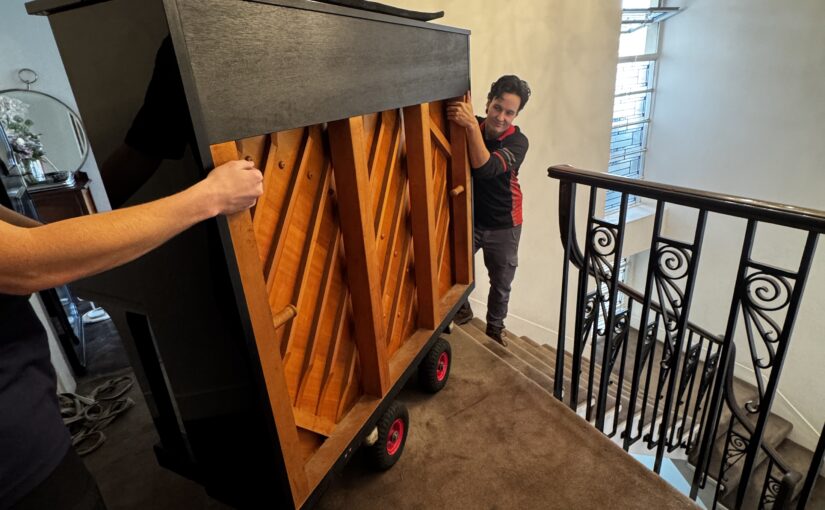 JM & SONS Piano Movers handling a heavy upright piano on specialist moving equipment near stairs in Melbourne
