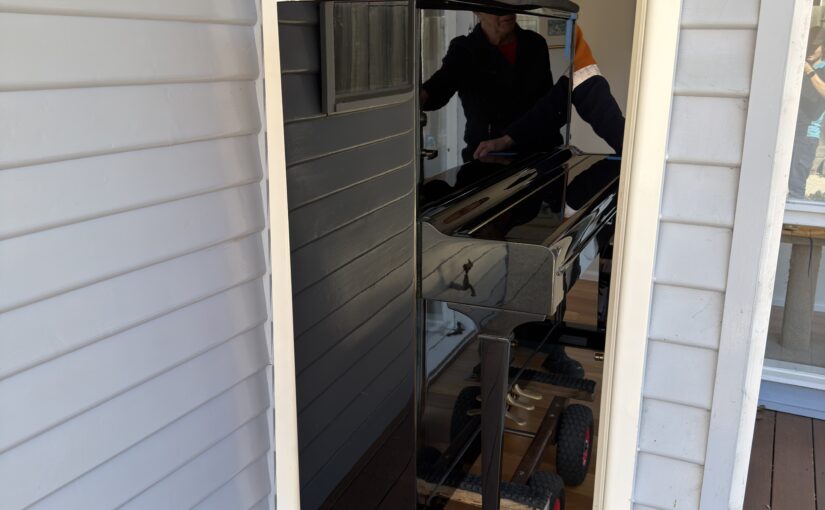 JM & SONS Piano Movers carefully moving a large upright piano through a narrow residential doorway in Melbourne