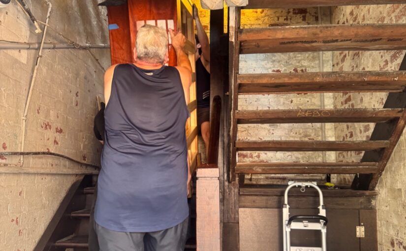 JM & SONS Piano Movers carefully moving a large upright piano through a very tight timber staircase in Melbourne